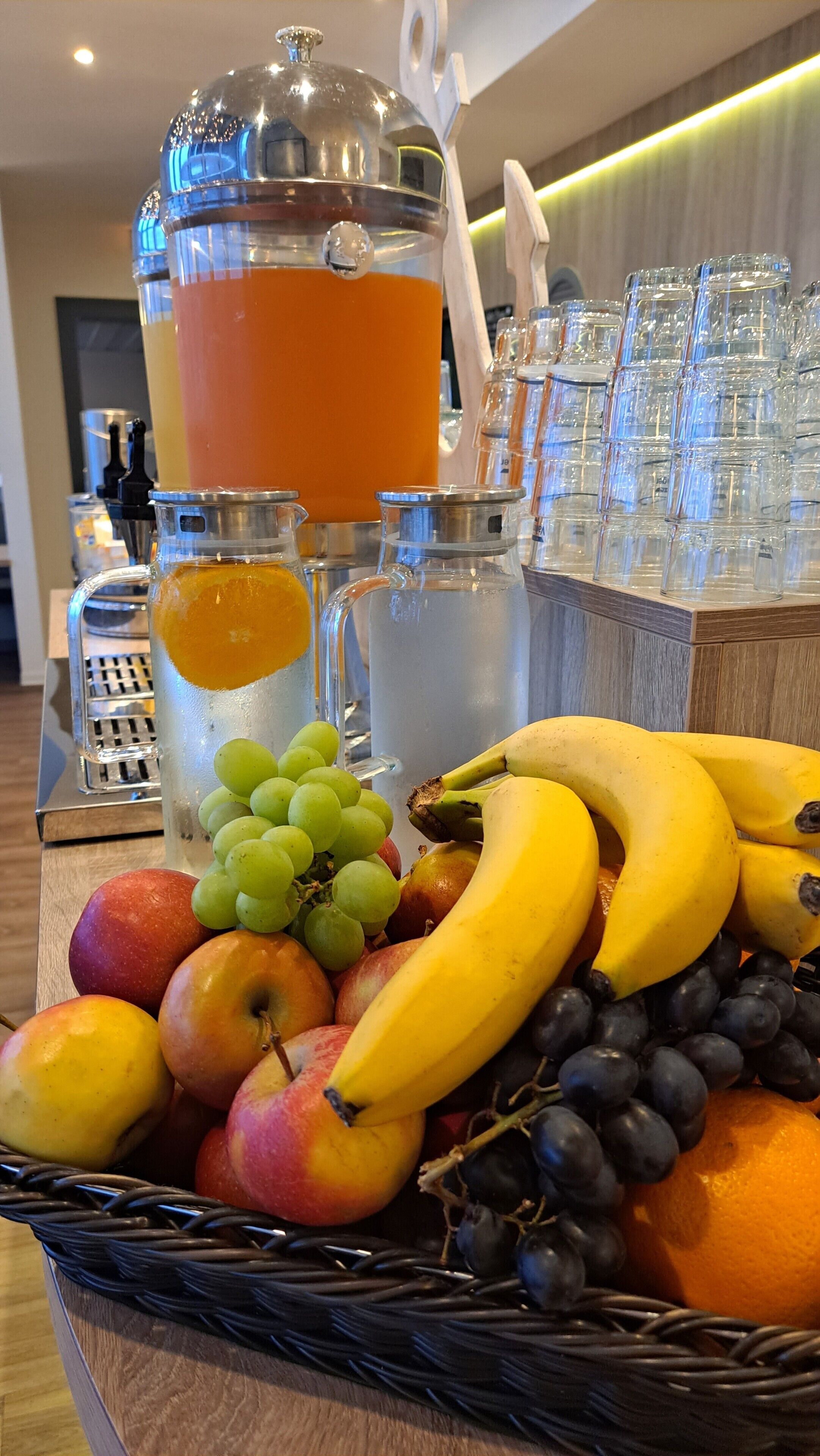 Un bufé de desayuno con frutas, un bol de ponche y un dispensador de zumo.