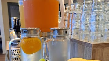 Un bufé de desayuno con frutas, un bol de ponche y un dispensador de zumo.