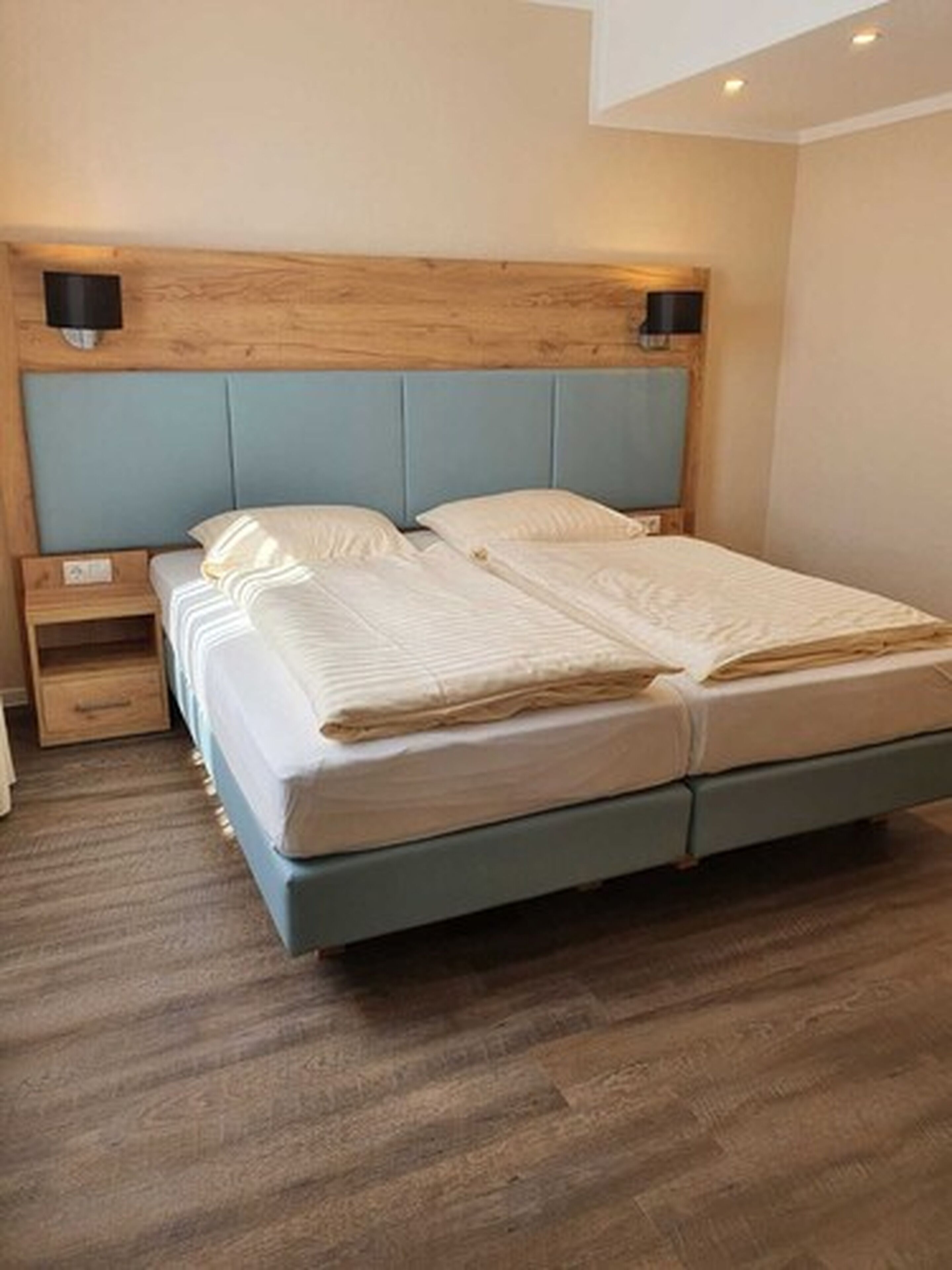Un dormitorio con cama, cabecera de madera, mesita de noche y un cajón pequeño.