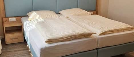 A bedroom with a bed, wooden headboard, nightstand, and a small drawer.