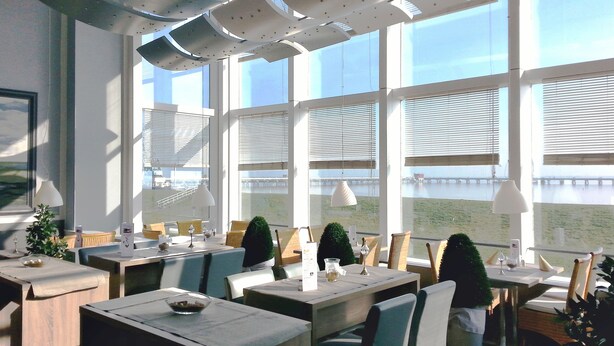 Un comedor moderno con amplias ventanas, mesas y sillas de madera.