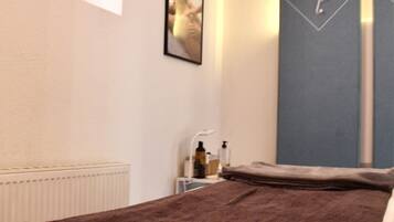 Una habitación de hotel con cama, un radiador, una planta pequeña, un cuadro enmarcado y una pared azul con un reloj.