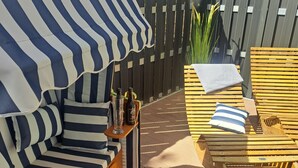Una terraza de madera con sillas de lounge a rayas y un banco acolchado con dosel a rayas.