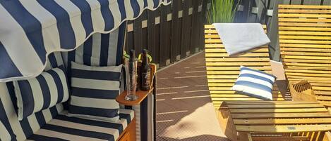 Une terrasse en bois avec des chaises longues à rayures et un banc rembourré surmonté d’un auvent à rayures.