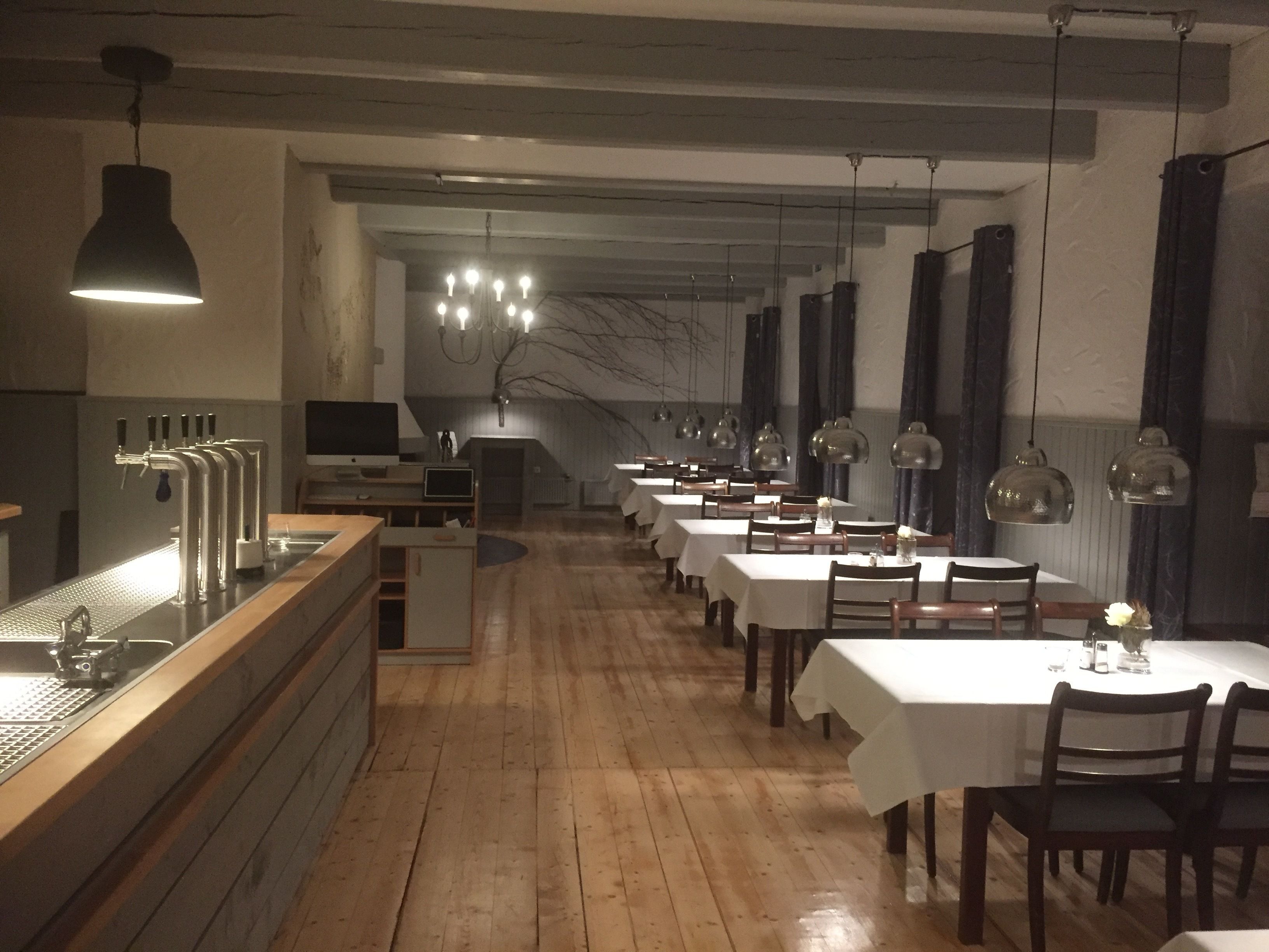 Un restaurant amb sòcols de fusta, tovallons blancs i lluminàries penjants.
