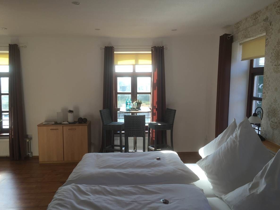 A hotel room with a large bed, a small desk with a chair, and a window with curtains.