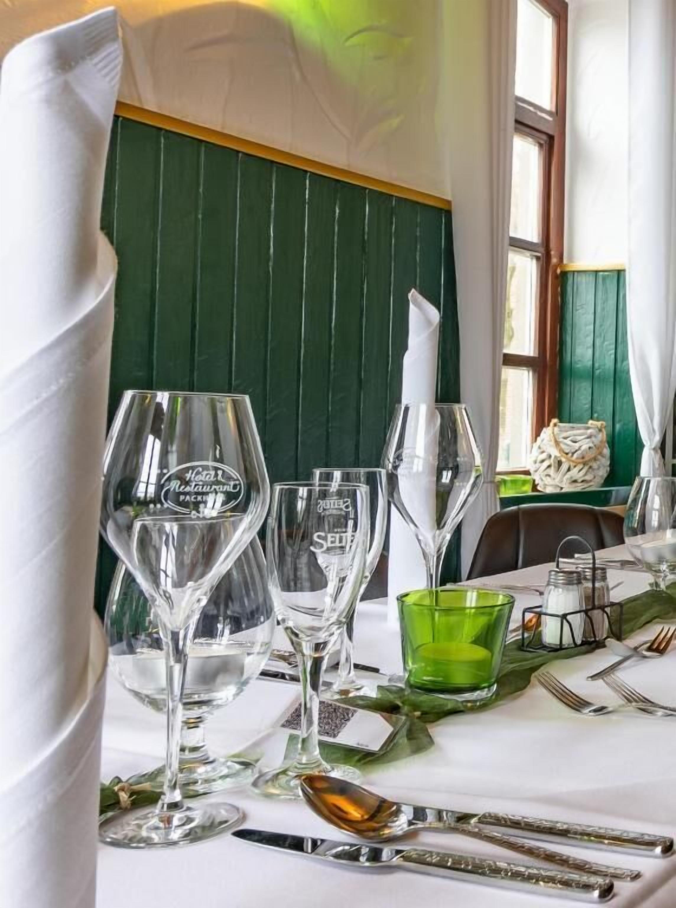 A dining table set with wine glasses, a green glass, and cutlery.