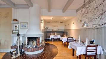 Um restaurante com lareira central, soalho em madeira e toalhas de mesa brancas.