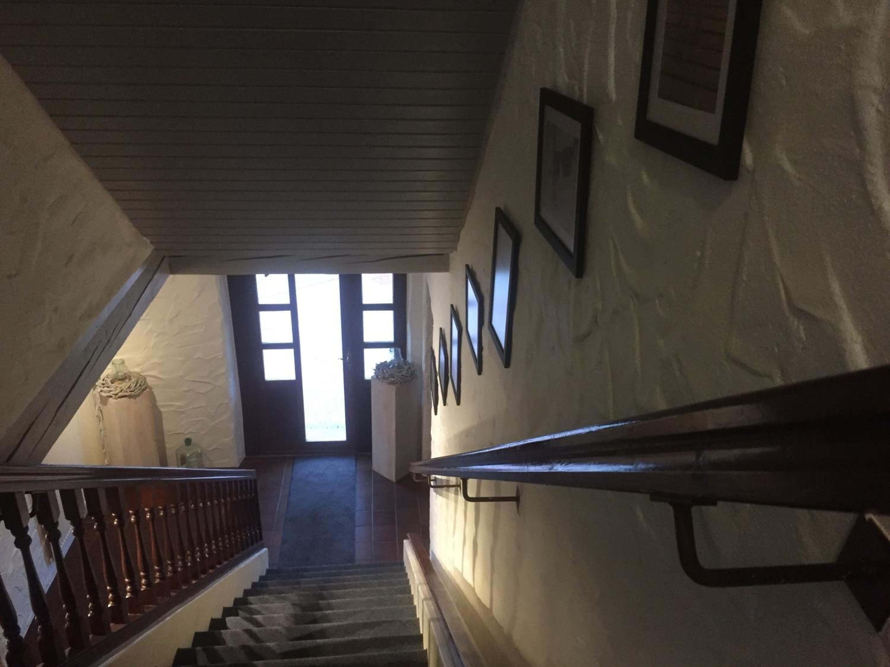 A staircase with a wooden handrail, a white wall with framed pictures, and a door at the top.