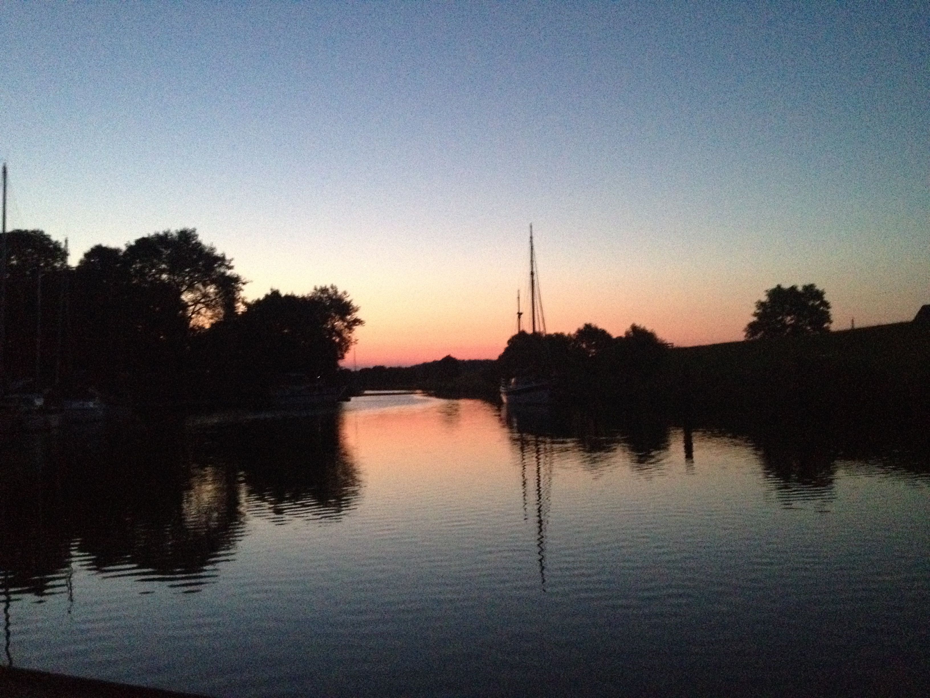 A calm river at dusk with boats and trees along the banks.