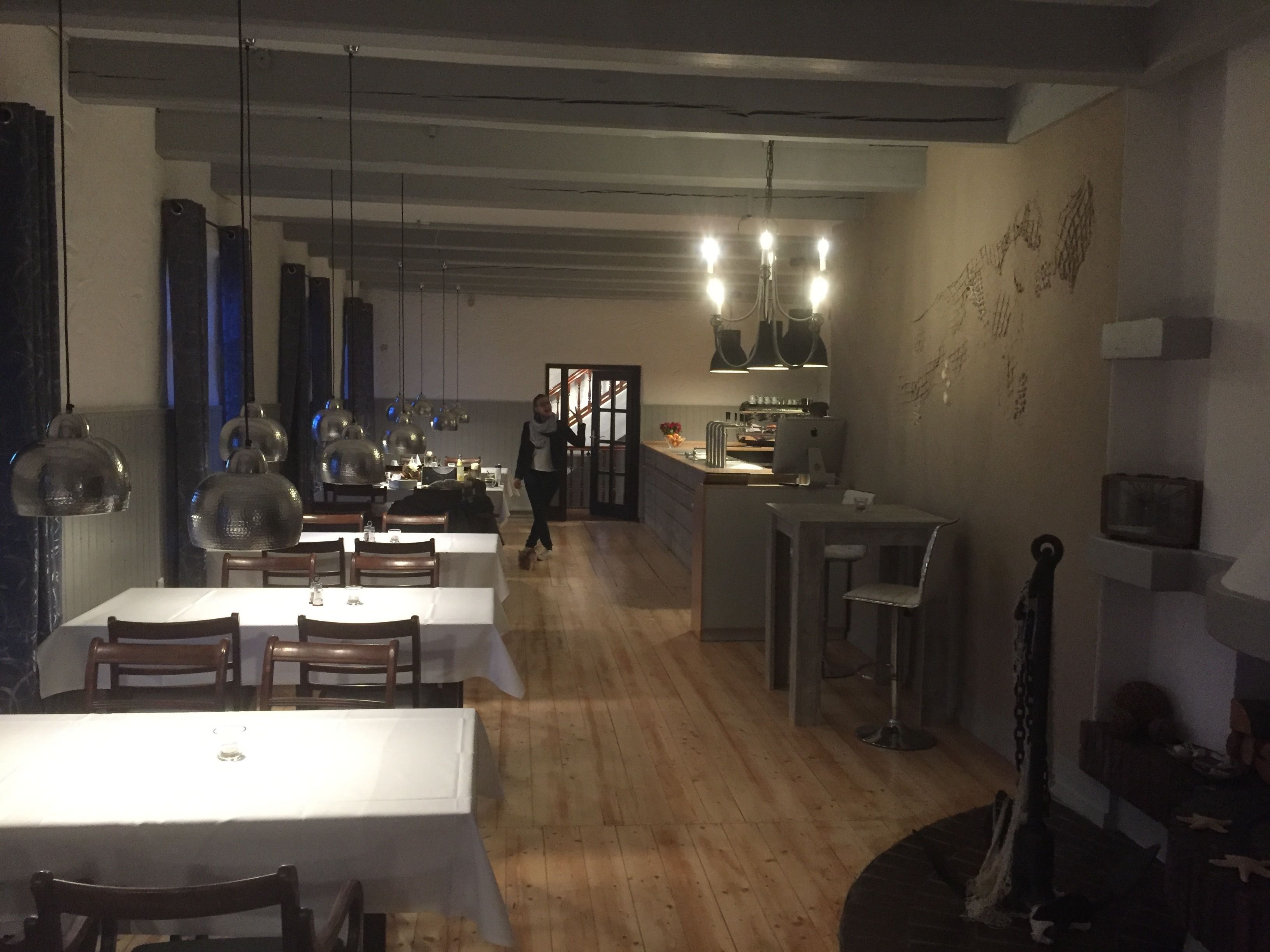 Un restaurante con suelo de madera, mesas blancas y lámparas colgantes.