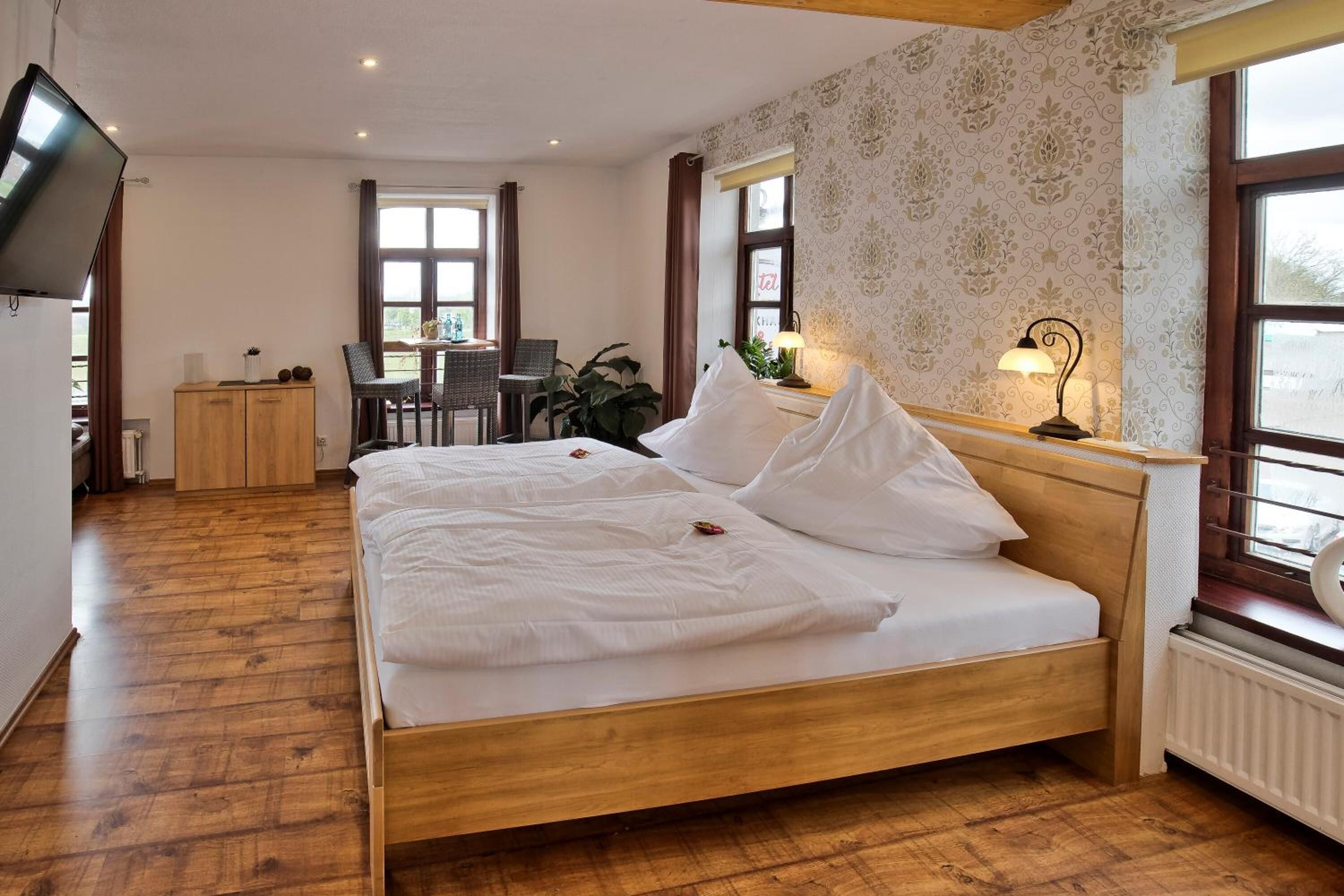 Un dormitorio con una cama de madera, un televisor montado en la pared, un escritorio con una silla y una ventana con cortinas.