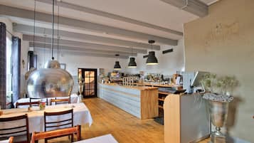 Un restaurant avec des tables et des chaises en bois, un coin bar avec un comptoir, des luminaires suspendus et une plante décorative.
