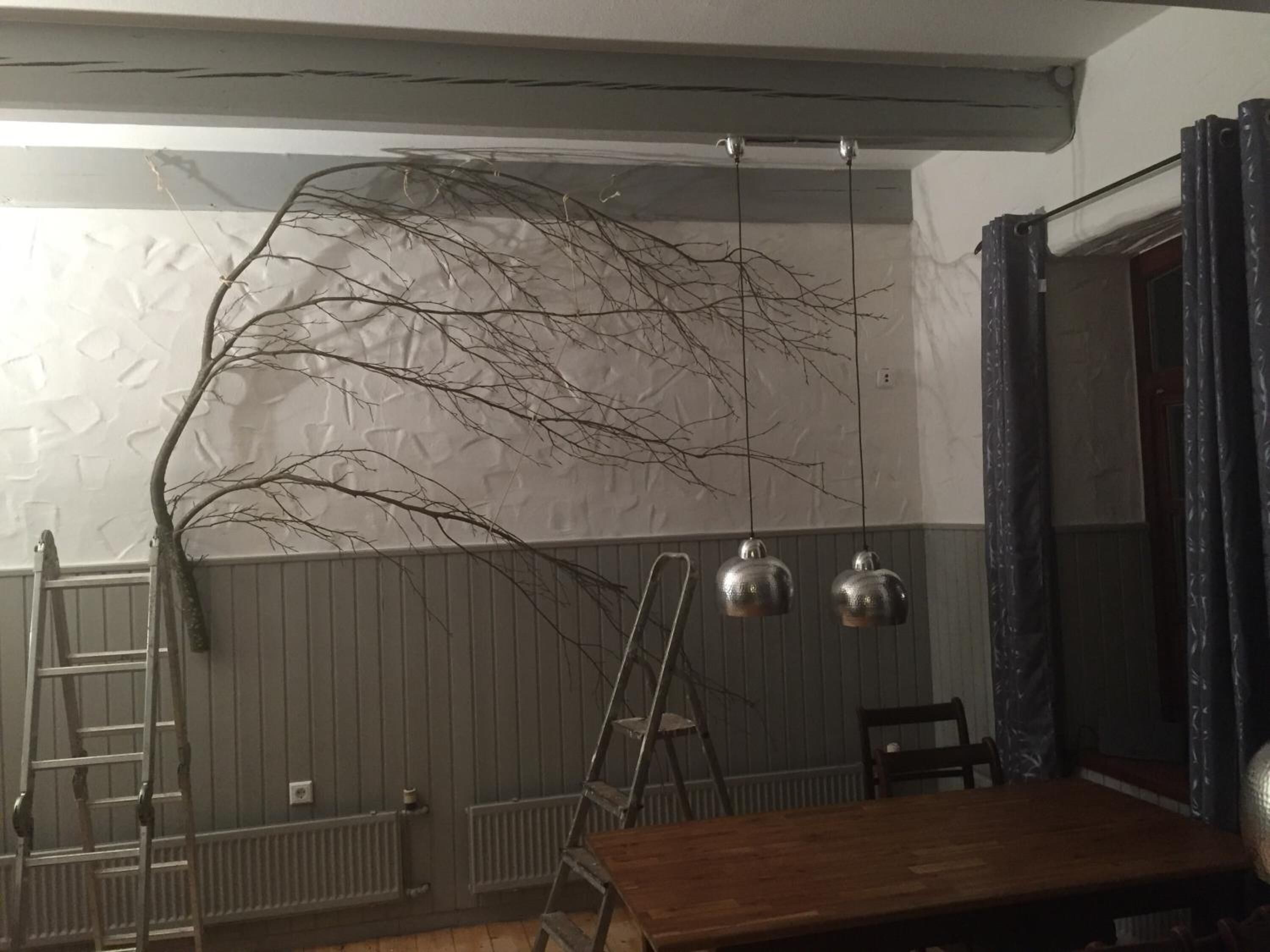 Ein Zimmer mit einem Holztisch, einer Leiter und einem hängenden Ast.