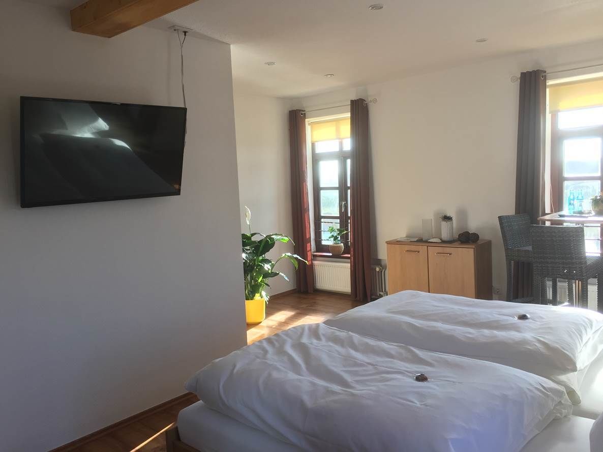 A bedroom with a bed, a TV mounted on the wall, a desk, and a chair.