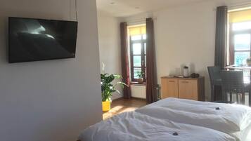 A bedroom with a bed, a TV mounted on the wall, a desk, and a chair.