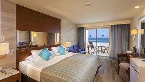 Ein Hotelzimmer mit einem großen Bett, einem Schreibtisch, einem Sessel und Blick auf den Ozean durch die Balkontüren.