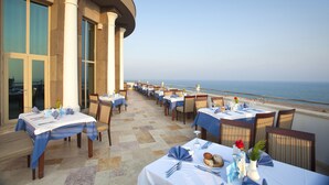 Ein Restaurant am Meer mit Außenbereich, Tischen mit blauen Tischdecken und Blick auf den Ozean.