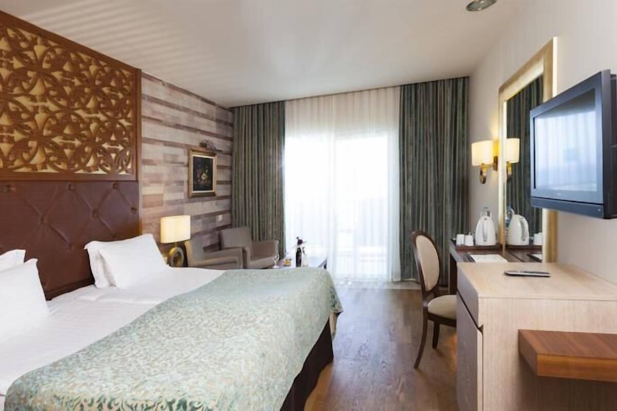A hotel room with a large bed, a desk with a chair, a television, and a decorative wall panel.