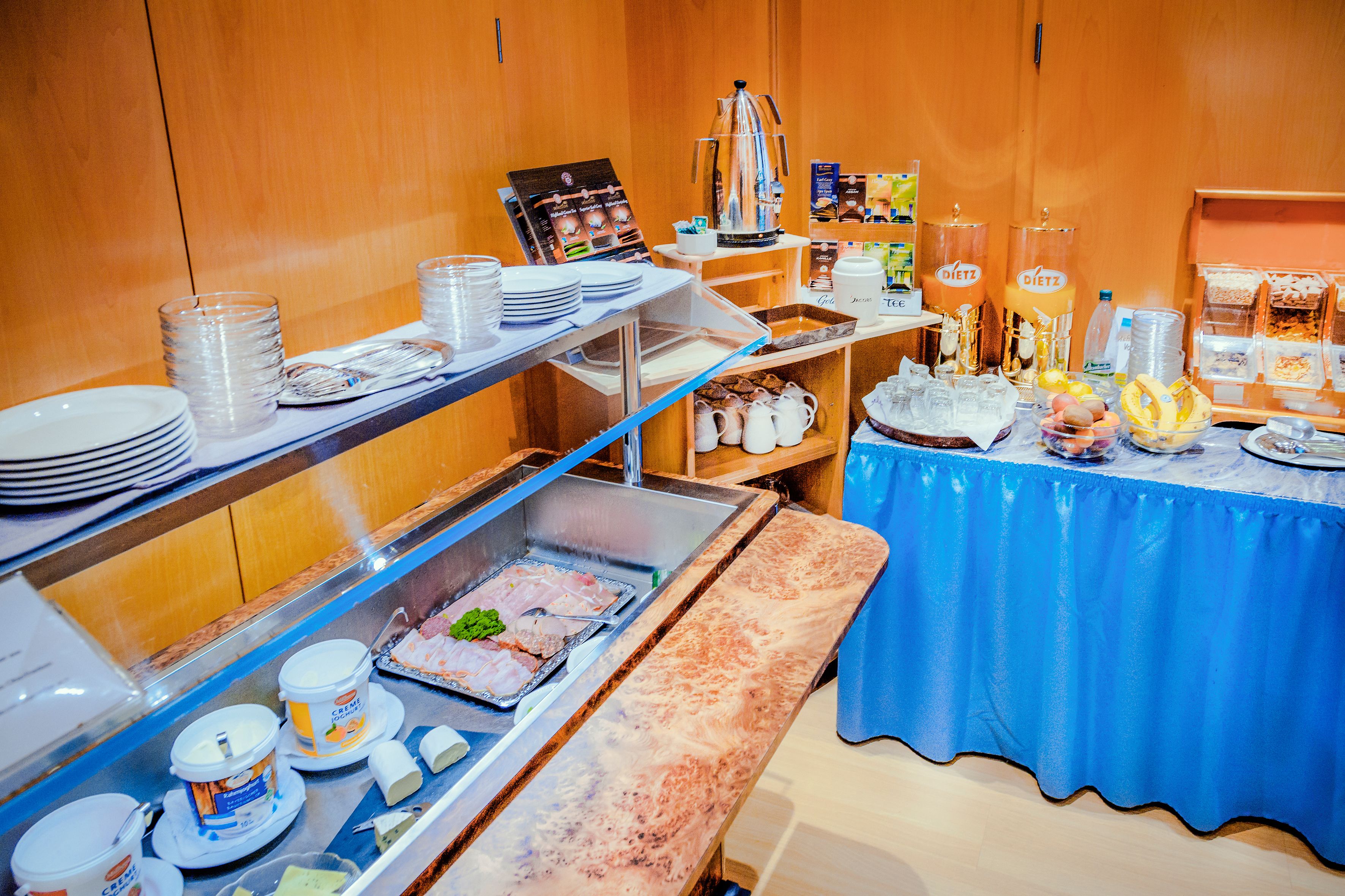 A buffet setup with various food items, including a coffee station, trays of food, and a blue-covered table.
