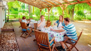 Un espacio comedor al aire libre cubierto, con sillas y mesas de madera, rodeado de vegetación.