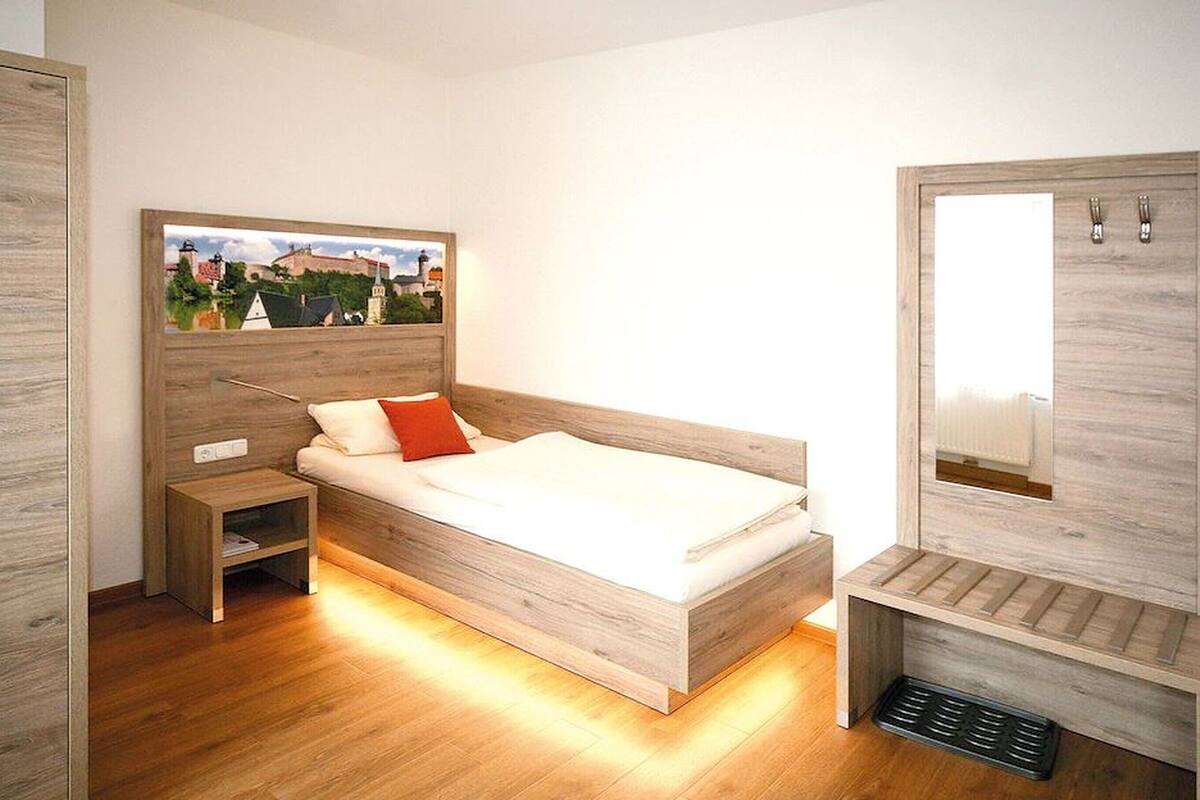 Ein modernes Schlafzimmer mit einem hölzernen Bett, einem Nachttisch, einem Kleiderschrank und einem großen Fenster mit Blick auf Gebäude.