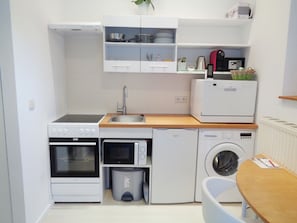 A compact kitchen with a stove, oven, microwave, sink, and a small washing machine. - Apartment Puell (Ingersleben)