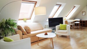 A modern loft-style living room with a sofa, armchairs, a coffee table, and a TV. There are skylights and a dining area visible. - Apartment Puell (Ingersleben)