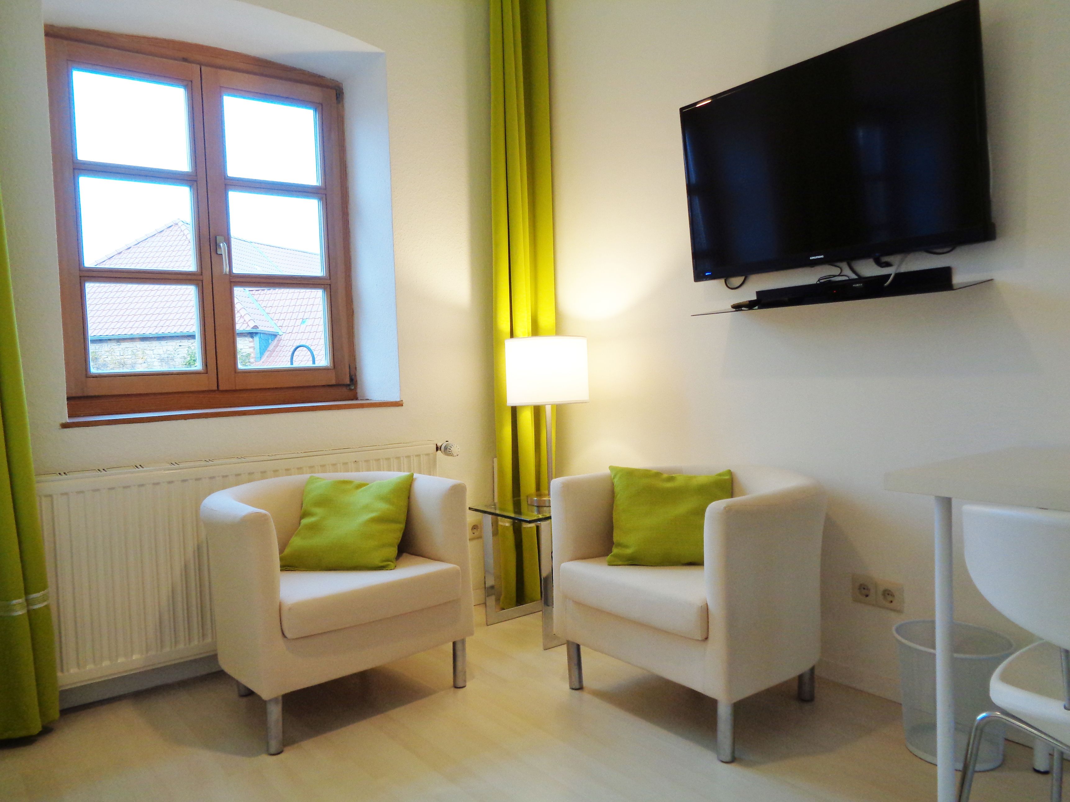 A room with two armchairs, a TV mounted on the wall, a window with curtains, and a radiator.