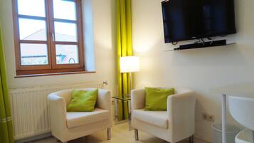 A room with two armchairs, a TV mounted on the wall, a window with curtains, and a radiator.
