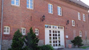A red brick building with multiple windows and a large white door. - Apartment Puell (Ingersleben)