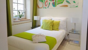 A hotel room with a bed, two bedside lamps, a window with a view, a radiator, and a green curtain. - Apartment Puell (Ingersleben)