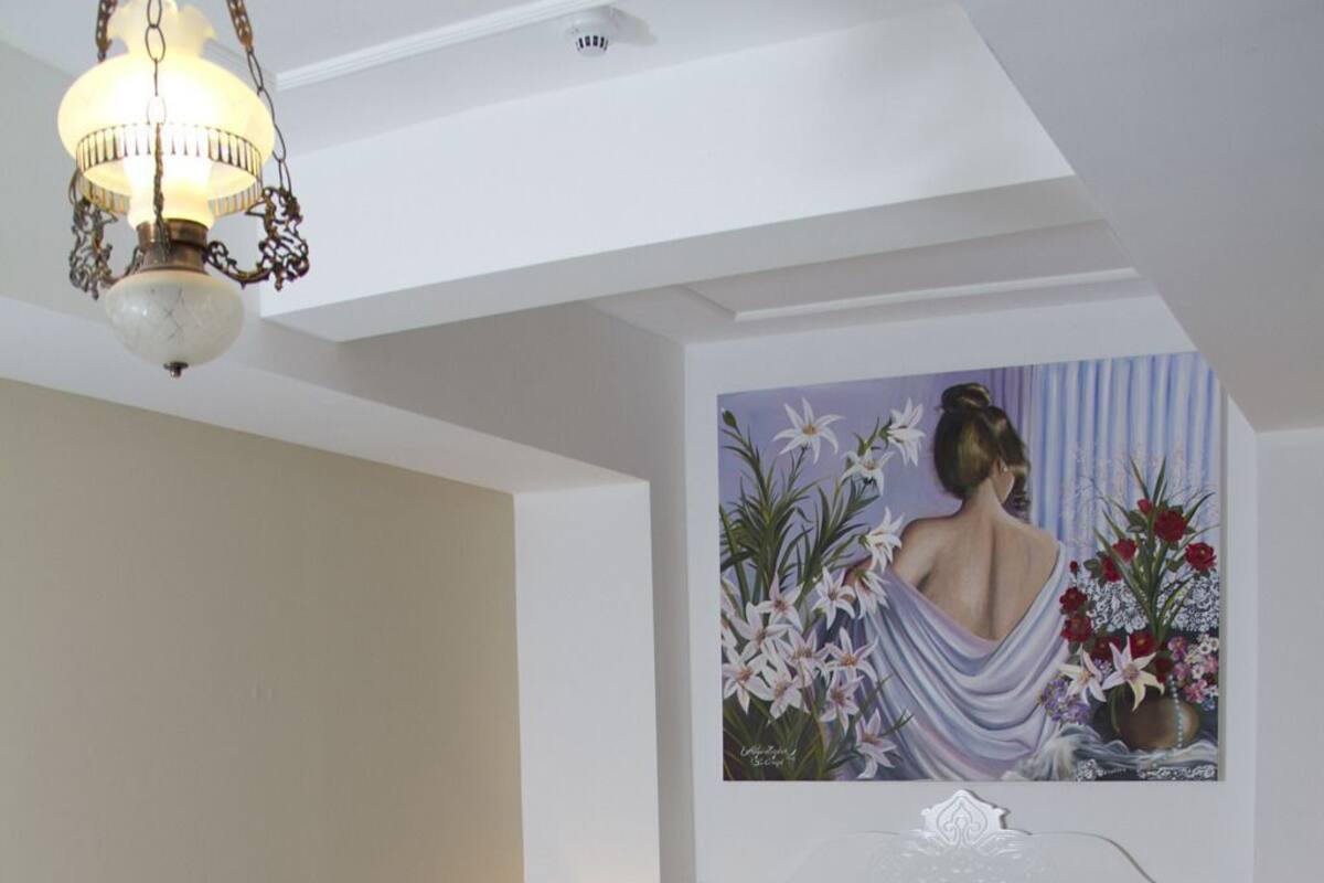 A bedroom with a bed, a nightstand, a lamp, a painting, and a chandelier.