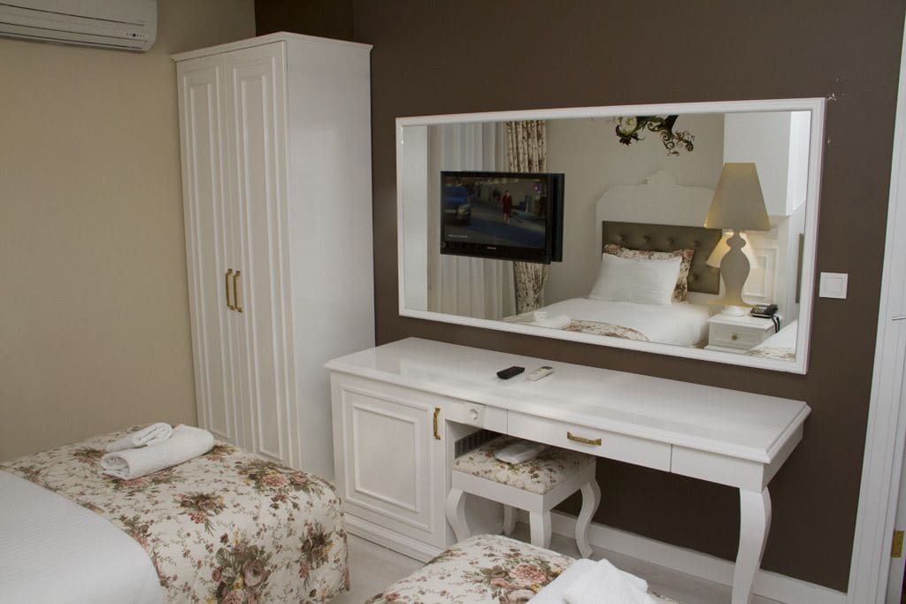 Un dormitorio con una cama, un aparador blanco, un espejo y un televisor.