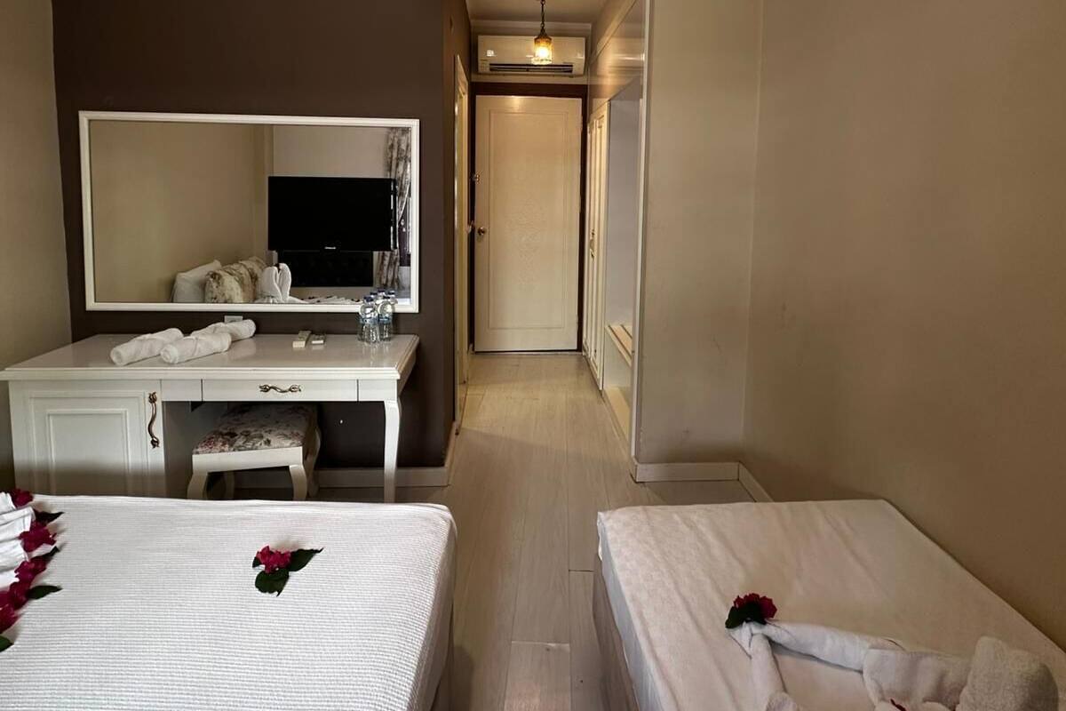 A hotel room with two beds, a vanity with a mirror, and a hallway leading to a door.
