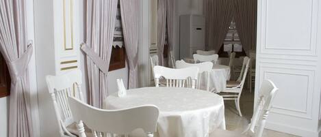 A formal dining room with white tables and chairs, elegant curtains, and classic chandeliers.