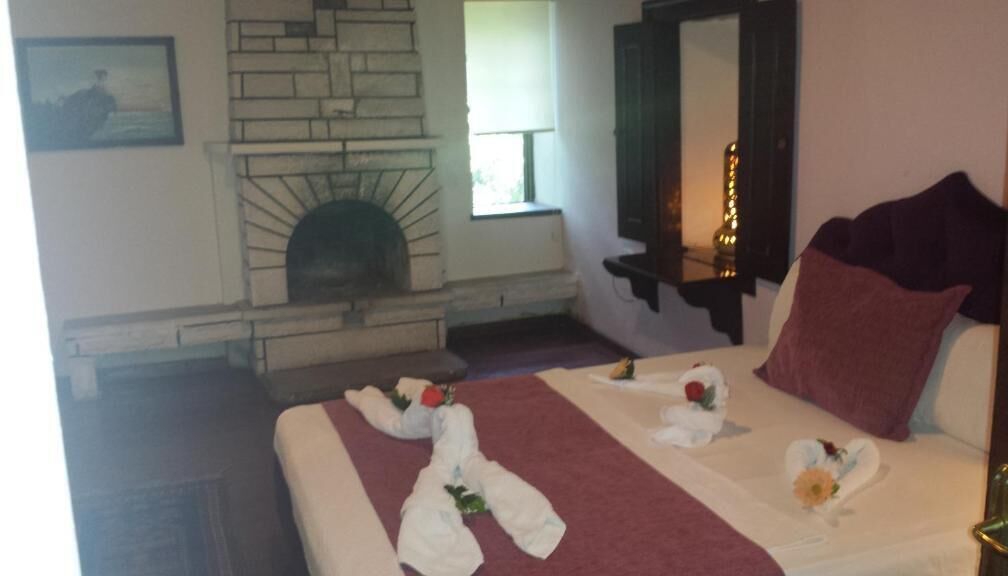 A hotel room with a stone fireplace, a bed with a red blanket, and a mirror above the bed.
