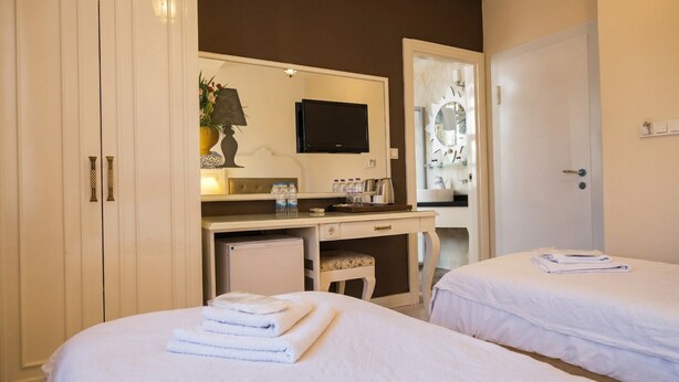 A hotel room with two beds, a desk with a flat-screen TV, a mirror, and a wardrobe. - Ozkavak Hotel Kaleici (Antalya)