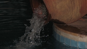 Una gran olla de barro rústica vertiendo agua en una piscina.
