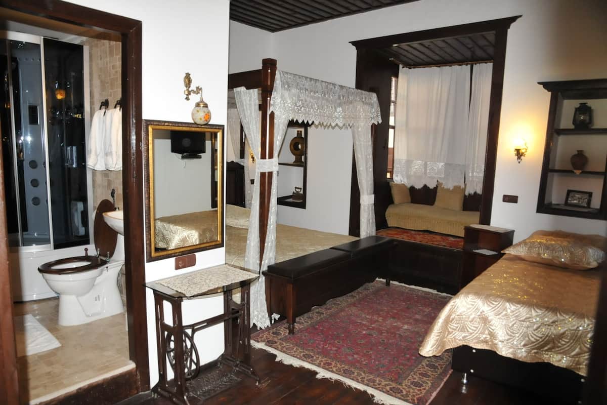 A bedroom with a four-poster bed, a sitting area with a sofa, a large mirror, and a wooden cabinet.