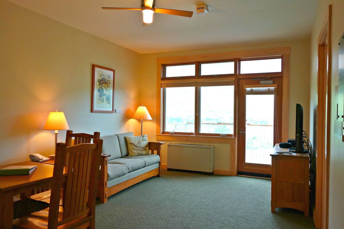 Ein gemütliches Wohnzimmer mit einer Couch, zwei Sesseln, einem Tisch, einem Deckenventilator und einem großen Fenster mit Aussicht.