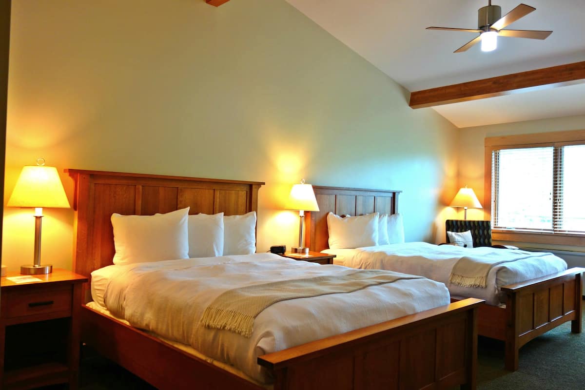 Ein Hotelzimmer mit zwei Betten, Holz Kopfteilen, Nachttischlampen, einem Deckenventilator und einem Fenster mit Jalousien.