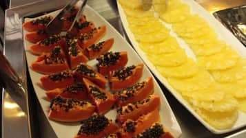 A buffet with sliced papaya and pineapple arranged on white plates.