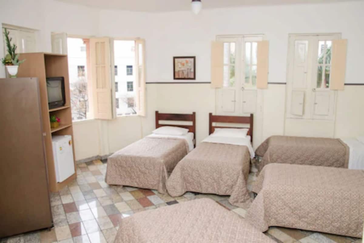 Une chambre avec quatre lits, une télévision, un réfrigérateur et une fenêtre avec des volets.