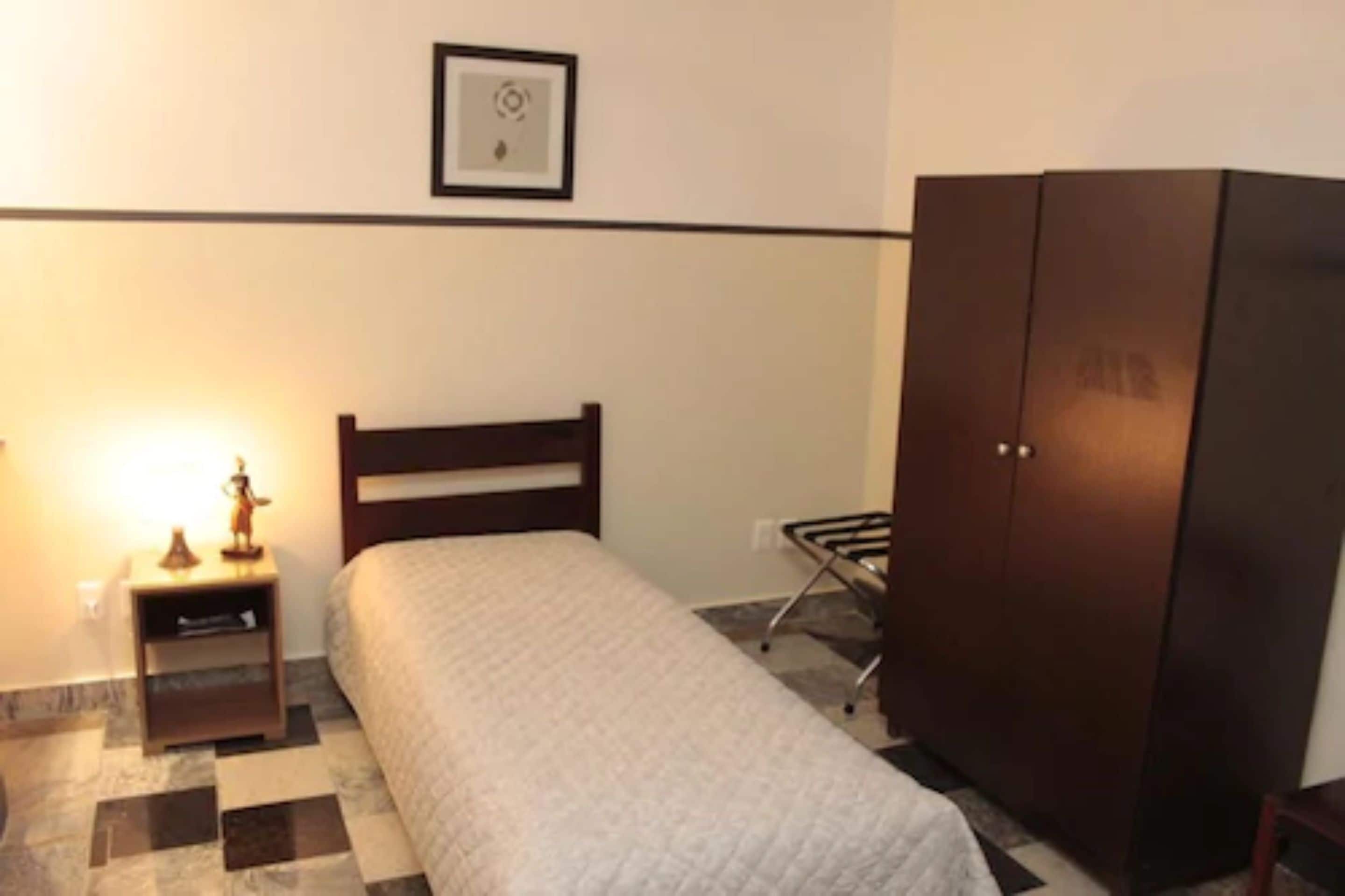 A bedroom with a bed, a nightstand, a wardrobe, and a wall-mounted picture.