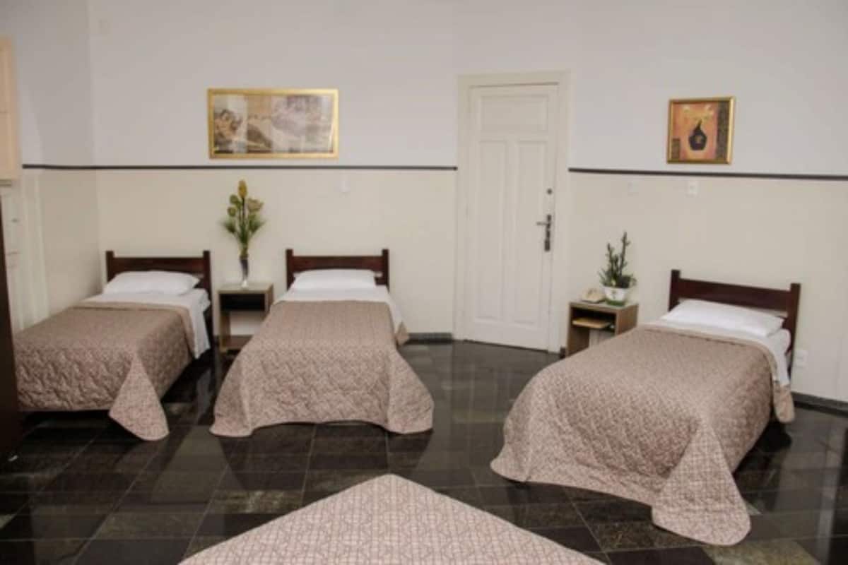 Une chambre d’hôtel avec trois lits, une porte et deux tableaux accrochés au mur.