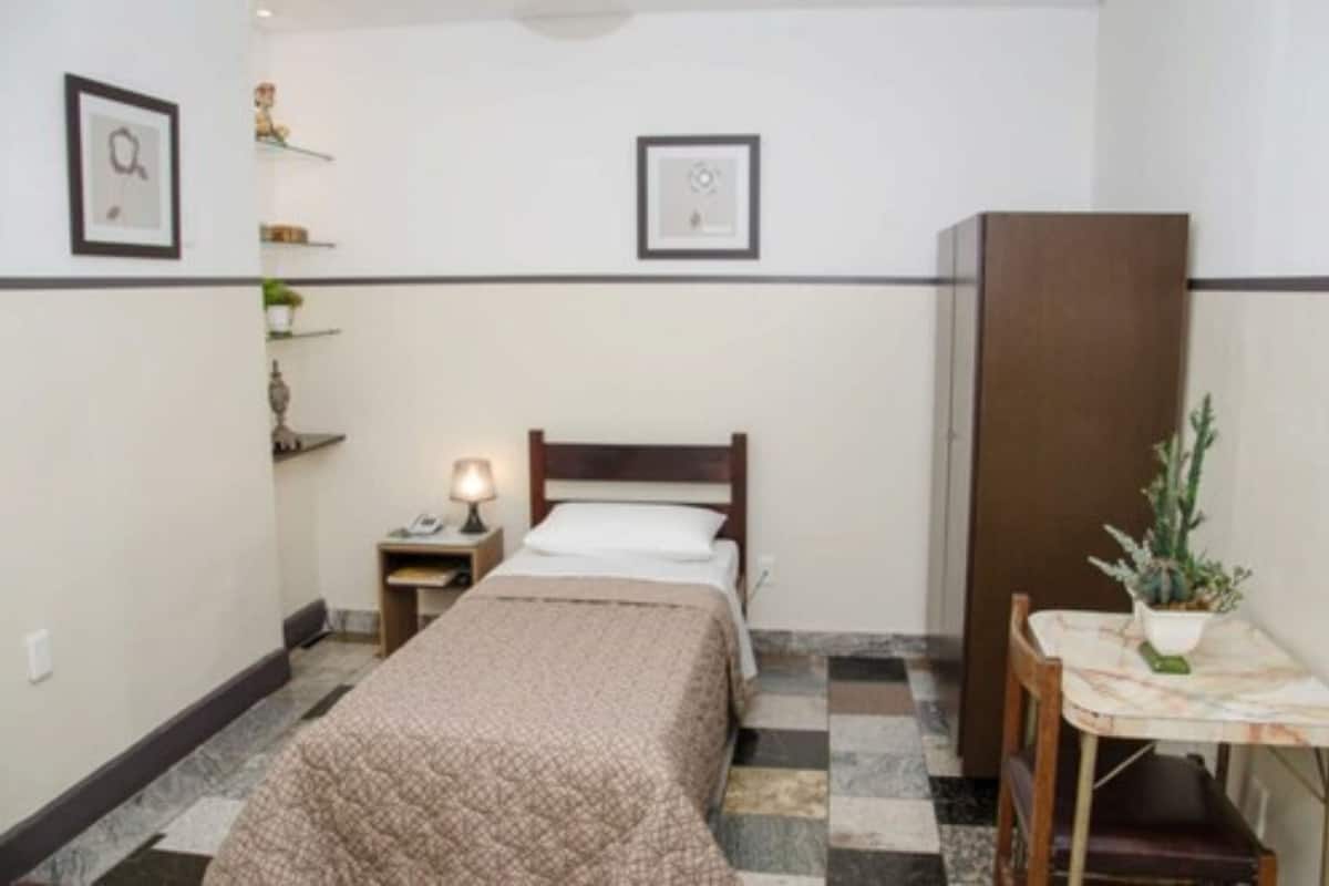 Une petite chambre à coucher, bien rangée, avec un lit, une table de chevet, une lampe et une plante en pot.