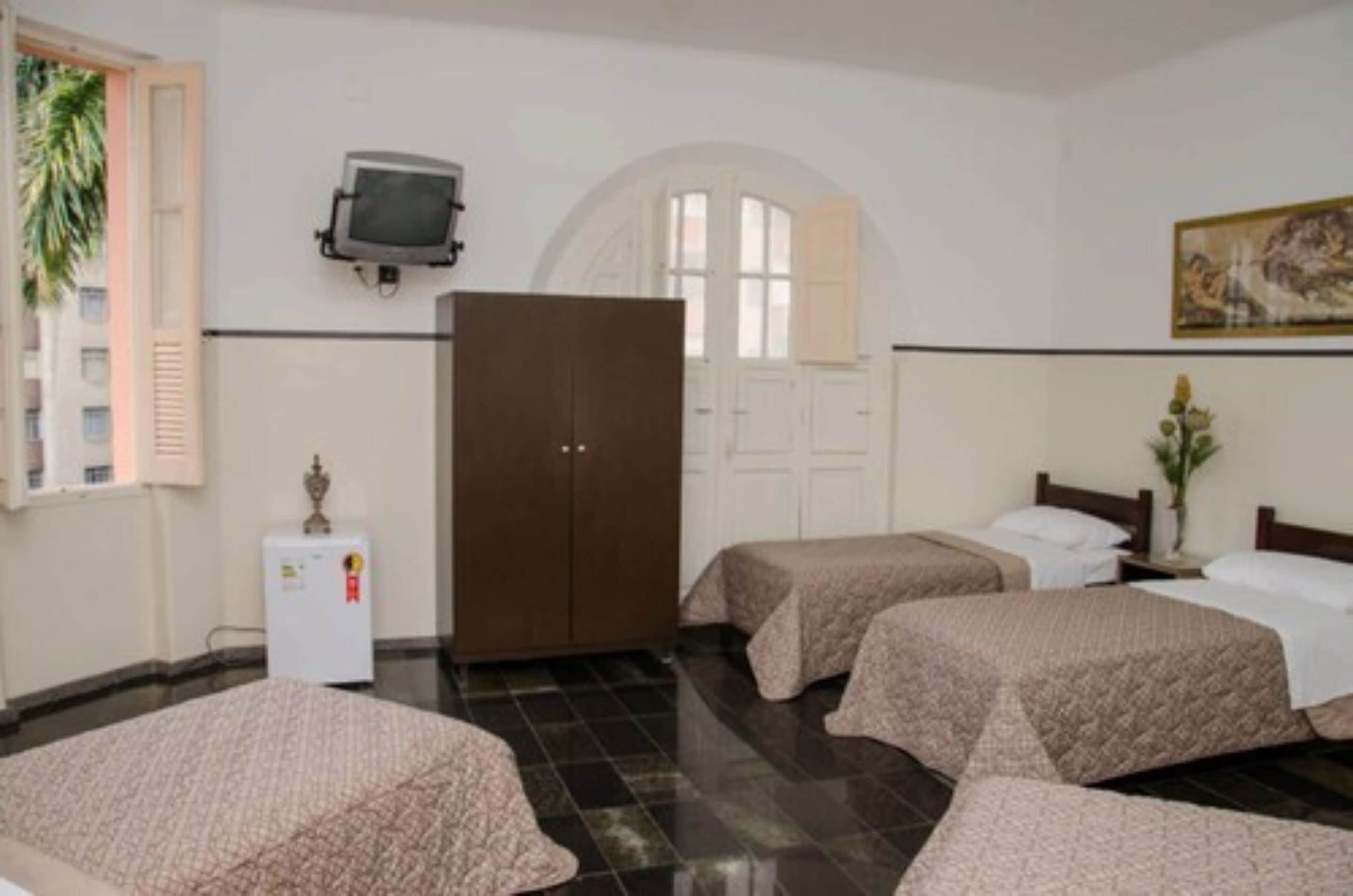 A hotel room with two beds, a wardrobe, a television, and a painting on the wall.