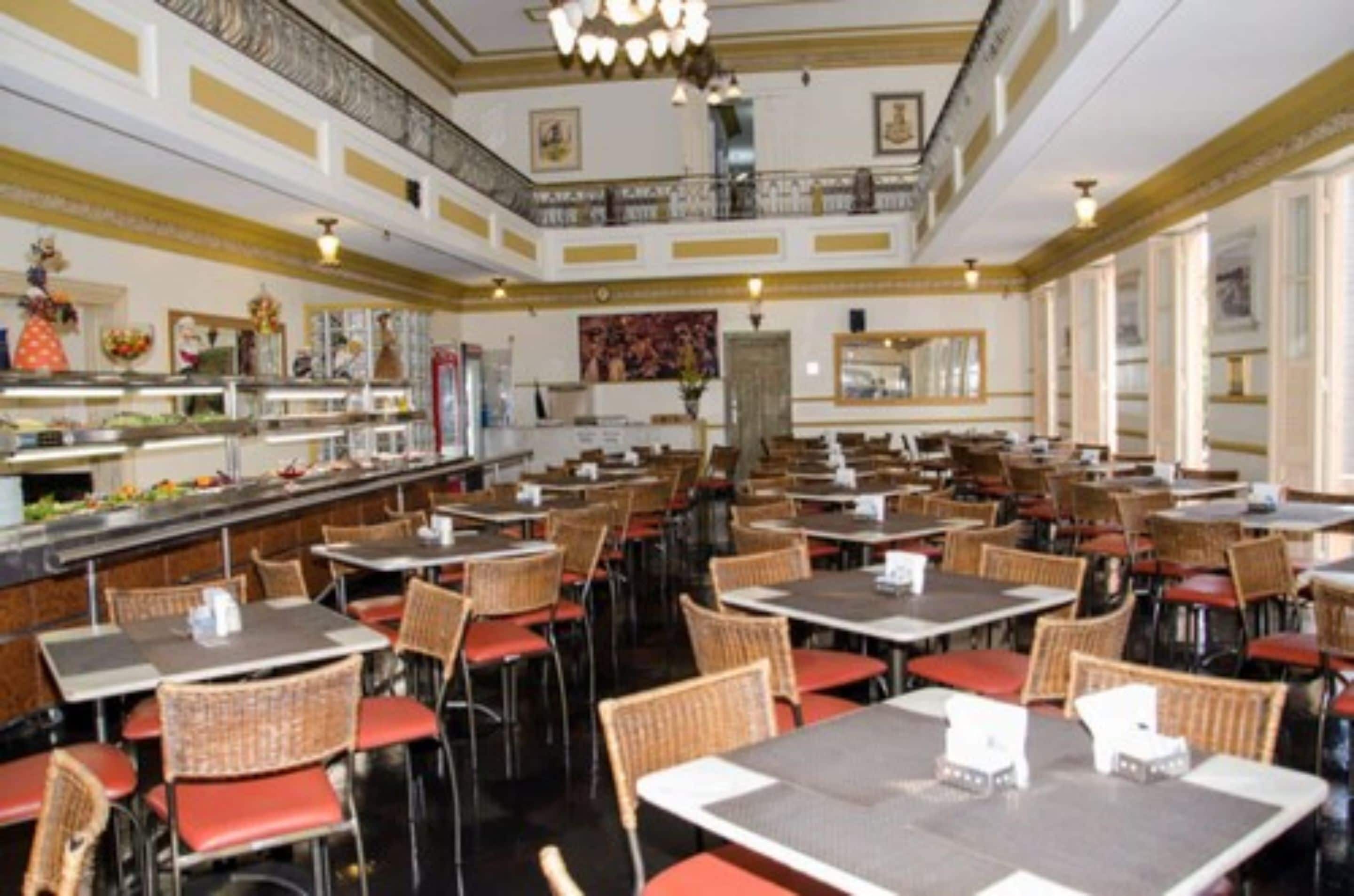 Een ruime eetruimte met meerdere tafels en stoelen, een buffet en een decoratief plafond.