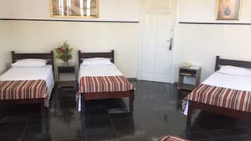 Quarto de hotel com duas camas, uma porta e uma pequena mesa com abajur.